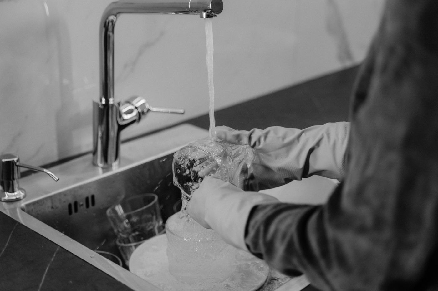 A person quietly washes a drinking glass under running water in a kitchen sink.