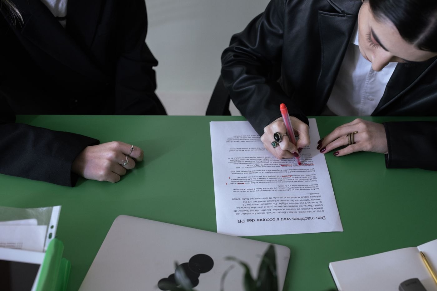 A hand marks words on a printed draft with a red pen.
