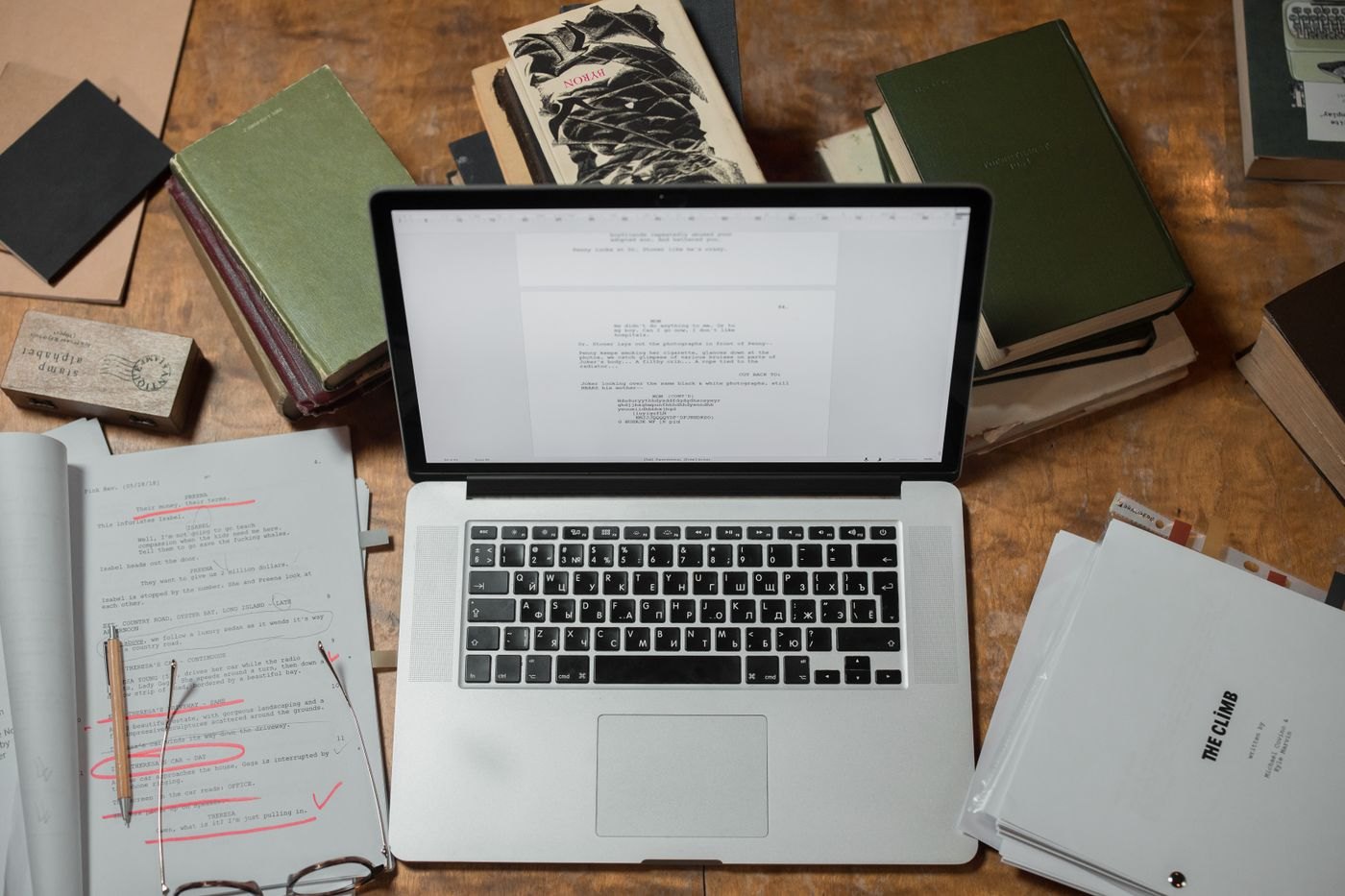 A laptop surrounded by loose script pages and reference books.