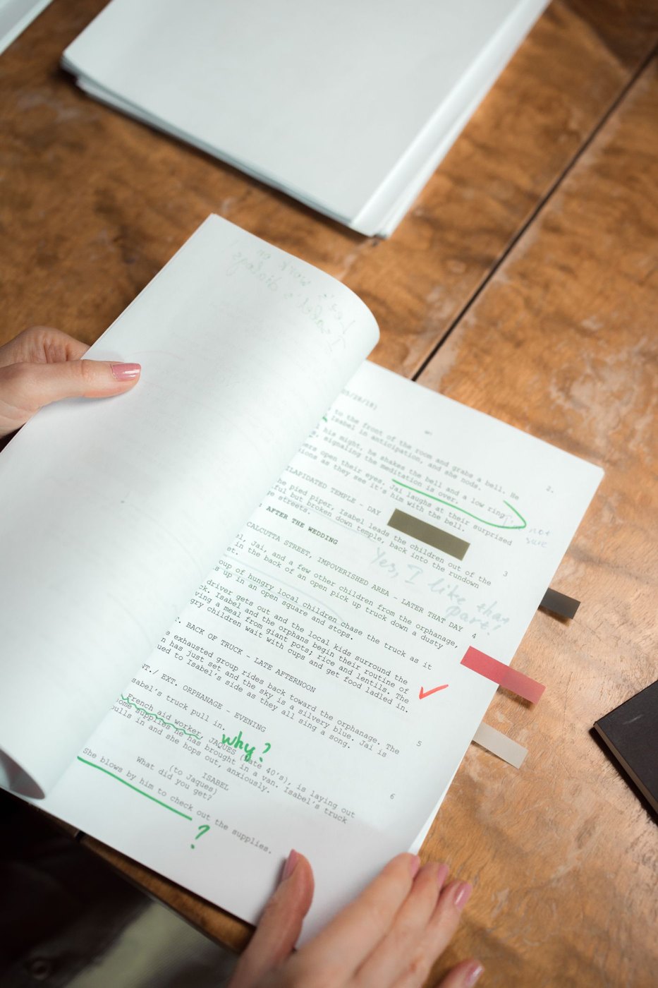 Hands hold annotated script pages above a wooden table.