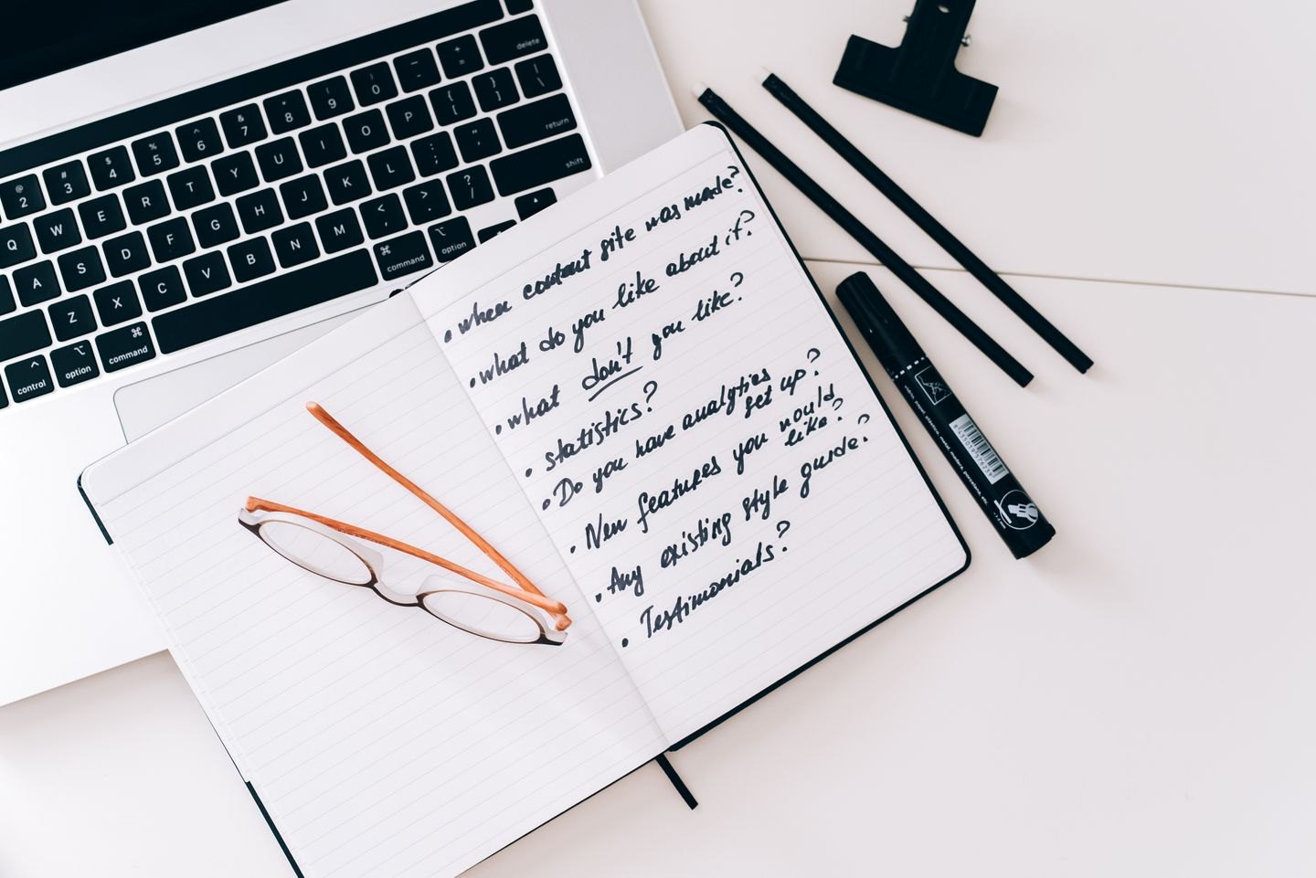 Handwritten questions in a notebook beside a laptop